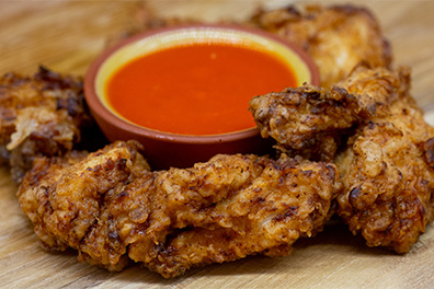 A ring of West Berlin Chicken Strips around a small bowl of dipping sauce.